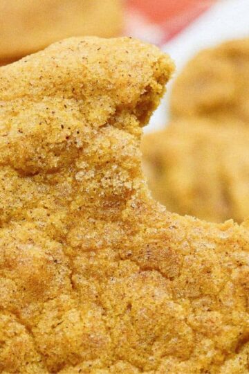 A person holding a pumpkin snickerdoodle with a bite taken out of it.