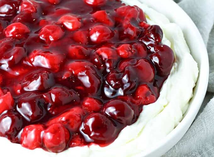 Cheesecake filling topped with cherries and served with cookies.