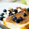 A close up image of apple butter spread on a piece of pound cake and topped with blueberries. Pound cake is on a simple white plate with an antique fork.