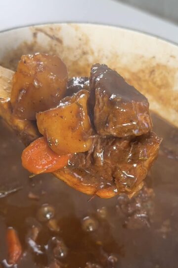 A spoon scoops beef stew out of the pot for serving.