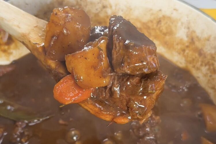 A spoon scoops beef stew out of the pot for serving.