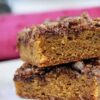 Two pieces of cinnamon maple blondies stacked on a plate, with a pink cloth in the background.