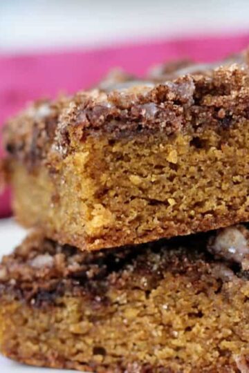 Two pieces of cinnamon maple blondies stacked on a plate, with a pink cloth in the background.