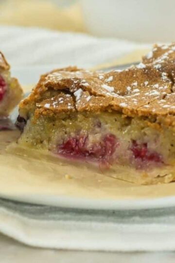 A slice of fruit-filled pie with a golden crust and powdered sugar sits on a plate, next to a partially eaten piece on a fork.