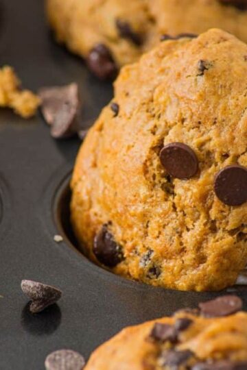 Peanut butter banana muffins in a baking tray, with some chocolate chips scattered around.