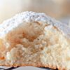 A close-up of a powdered sugar-coated cream cheese cookie with a bite taken out, resting on a wire cooling rack.