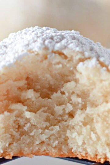 A close-up of a powdered sugar-coated cream cheese cookie with a bite taken out, resting on a wire cooling rack.