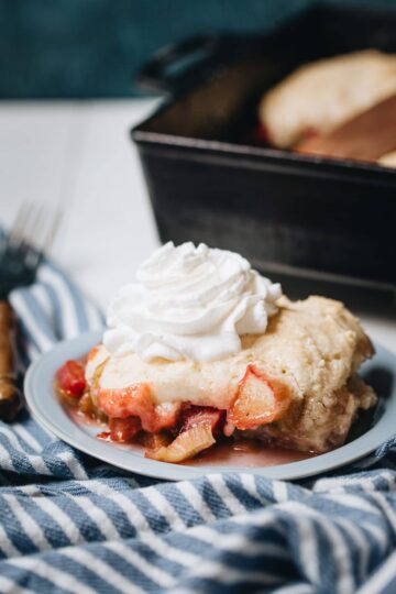 Side image of rhubarb cobbler on a plate with a cast iron baking dish in the background.