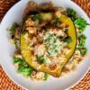 Acorn squash stuffed with kale, white beans, and cheese on a white plate, placed on a woven mat.