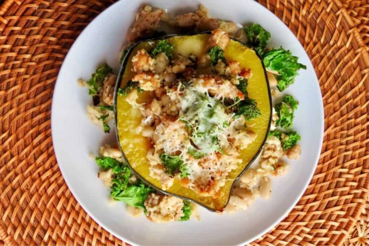 Acorn squash stuffed with kale, white beans, and cheese on a white plate, placed on a woven mat.