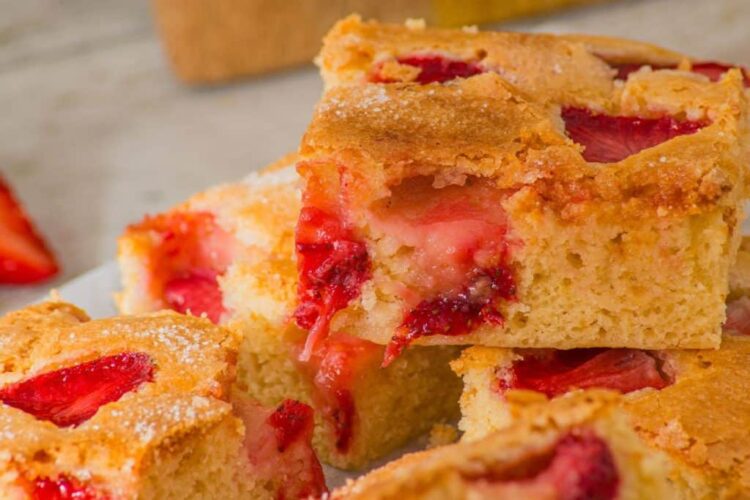 Close-up of strawberry sheet cake slices, showcasing a golden brown crust and vibrant chunks of strawberries.