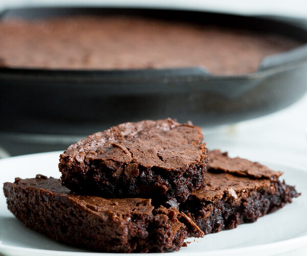 Close up image of three cast iron skillet brownies stacked on a white plate with the cast iron skillet in the background.