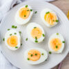 A white plate with six halved air fryer hard boiled eggs, each topped with chopped green chives, on a light wooden surface.