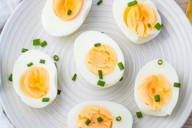 A white plate with six halved air fryer hard boiled eggs, each topped with chopped green chives, on a light wooden surface.