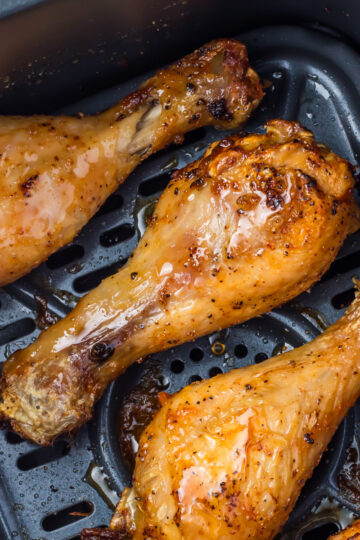 Close-up of three air fryer hot honey chicken drumsticks in an air fryer basket.