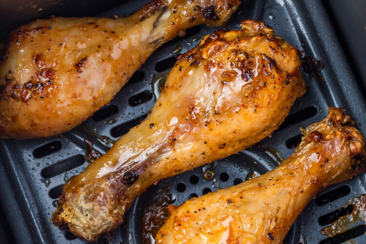 Close-up of three air fryer hot honey chicken drumsticks in an air fryer basket.