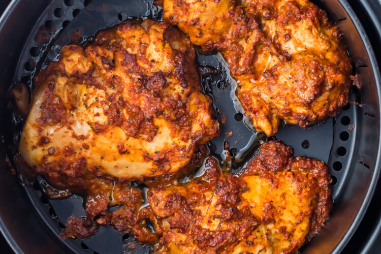 Cooked chicken pieces, seasoned with a reddish spice mix reminiscent of pollo asado, placed inside an air fryer basket. The chicken appears crispy and well-cooked.
