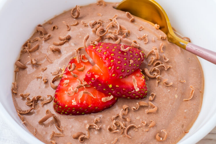 A white bowl filled with chocolate cottage cheese mousse, topped with sliced strawberries and chocolate shavings, with a gold spoon on the side.