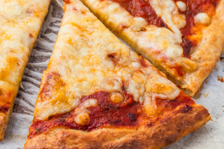 A close-up of cottage cheese pizza slices on parchment paper, showing melted cheese, tomato sauce, and a golden-brown crust.