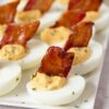 Deviled eggs with candied bacon sit on a serving platter for serving.