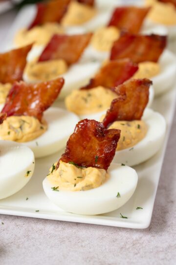 Deviled eggs with candied bacon sit on a serving platter for serving.