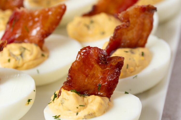 Deviled eggs with candied bacon sit on a serving platter for serving.