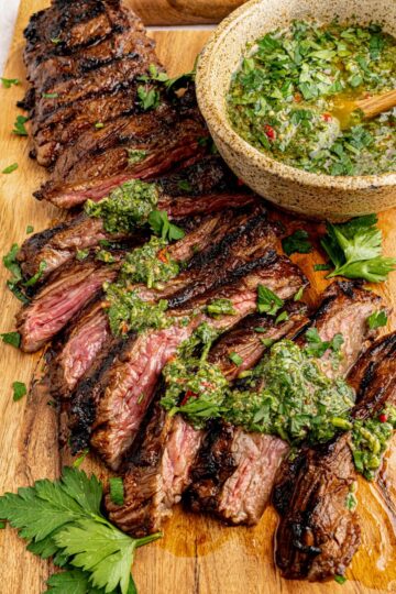 Easy grilled skirt steak is sliced with chimmichurri sauce on top for serving