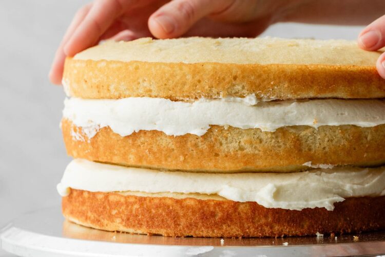 hands placing 3rd cake layer on top of a cake.