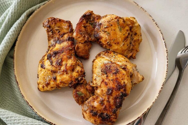 Three pieces of pan roasted chicken on a round plate with mint green napkin, fork, and knife on the background.