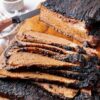 A baked brisket sliced on a wooden cutting board for serving.