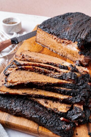 A baked brisket sliced on a wooden cutting board for serving.