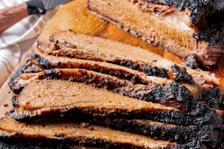 A baked brisket sliced on a wooden cutting board for serving.