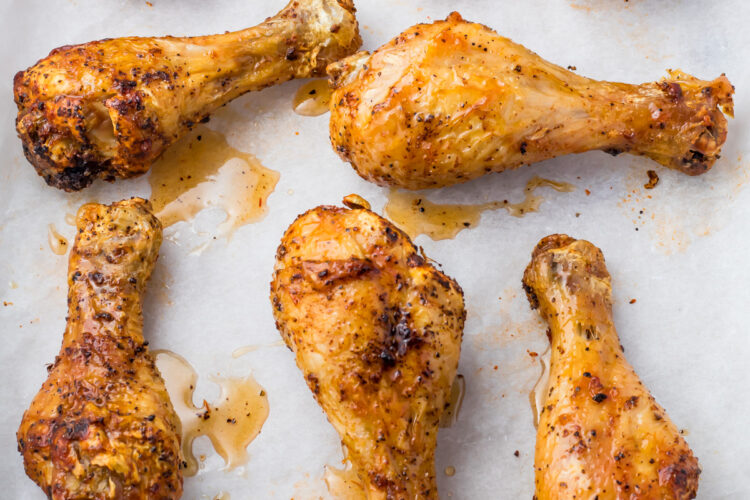 Oven baked drumsticks with a golden, crispy skin are arranged on a sheet of parchment paper. They appear well-seasoned, with visible spices and a slight glaze from their natural juices.
