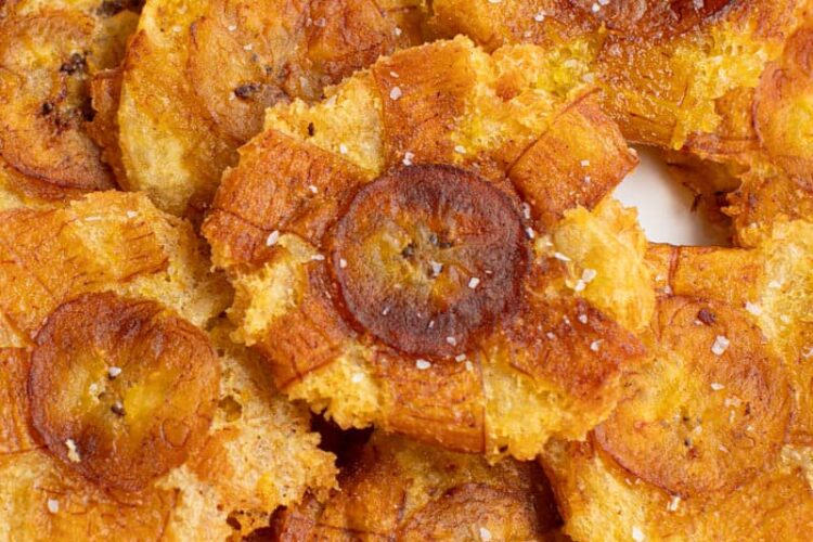 Tostones (fried green plantains) piled on a white plate for serving.