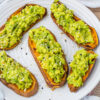 Slices of sweet potato avocado toast sprinkled with mixed seeds on a white plate.