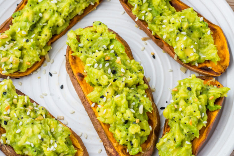Slices of sweet potato avocado toast sprinkled with mixed seeds on a white plate.