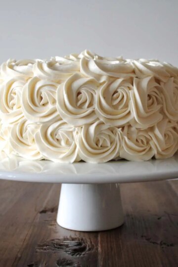 Cake decorated with buttercream rosettes on a white cake stand.
